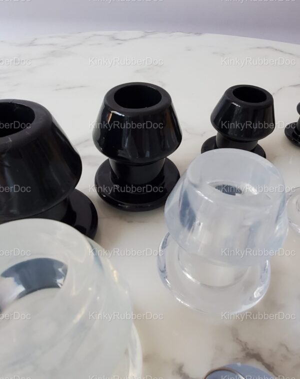 Close-up view of black and clear hollow plugs in multiple sizes, highlighting their smooth finish and structured design on a marble surface.