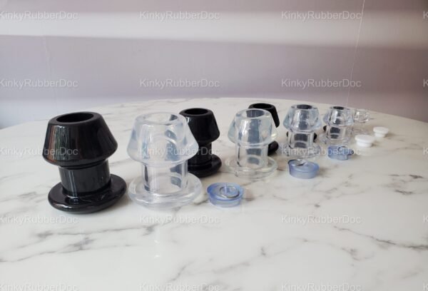 Set of black and clear hollow plugs in multiple sizes, each with removable silicone stoppers, displayed on a marble surface.