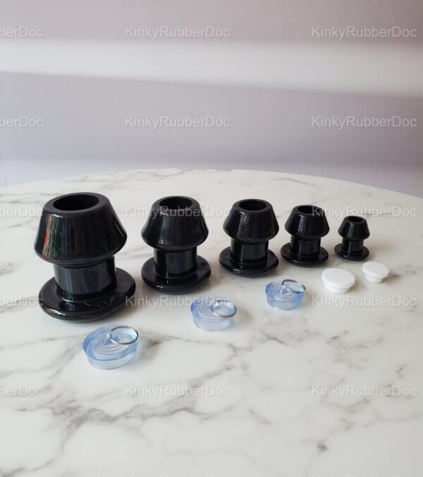 Collection of black hollow plugs in various sizes with removable silicone stoppers, displayed on a marble surface.