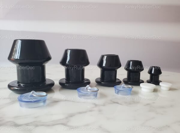 Set of black hollow plugs in various sizes with included silicone stoppers and removable caps, displayed on a marble surface.
