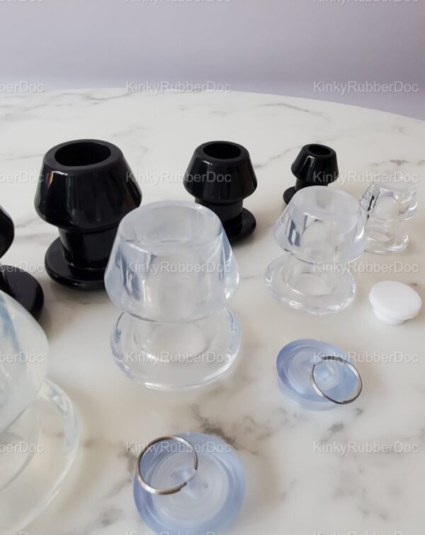 Angled close-up view of black and clear hollow plugs in various sizes, featuring removable silicone stoppers, displayed on a marble surface.