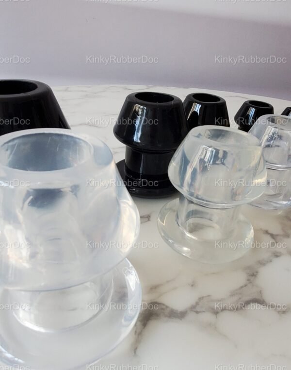Close-up view of black and clear hollow plugs in multiple sizes, displayed on a marble surface with a smooth finish.