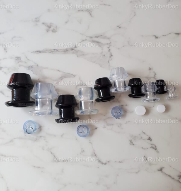 Top-down view of black and clear hollow plugs in various sizes, featuring removable silicone stoppers, displayed on a marble surface.