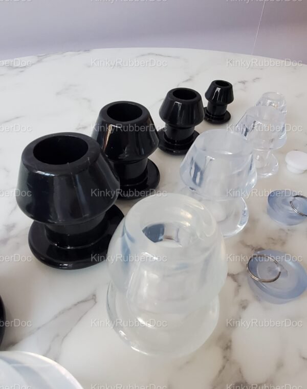 Angled close-up view of black and clear hollow plugs in multiple sizes, featuring smooth finishes and structured designs, displayed on a marble surface.