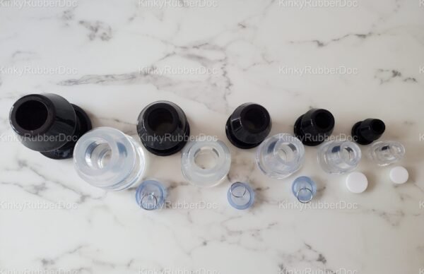 Top-down view of black and clear hollow plugs in multiple sizes, with removable silicone stoppers, displayed on a marble surface.