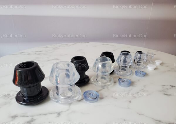 Collection of black and transparent hollow plugs in multiple sizes, with removable silicone stoppers, displayed on a marble surface.