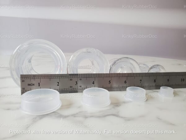 A lineup of clear TPE hollow plugs with matching stoppers, displayed alongside a ruler for precise size measurement.
