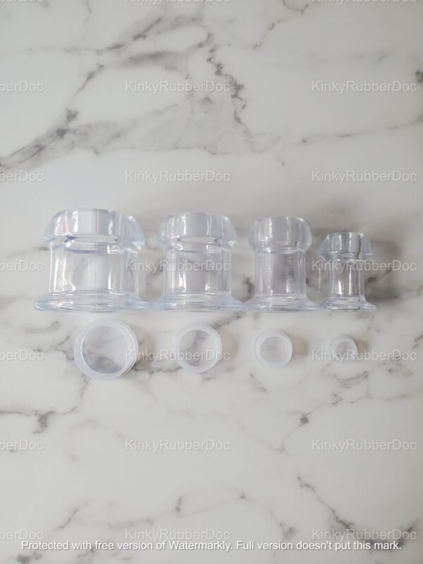 A set of clear TPE hollow plugs in multiple sizes, lined up on a marble surface with removable stoppers placed in front for size comparison.