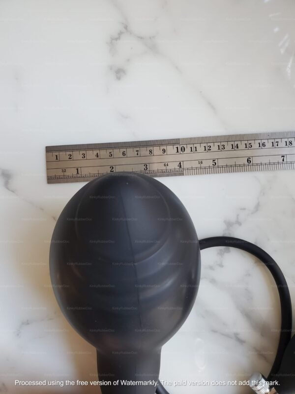 A fully expanded extra-large inflatable silicone butt plug, placed next to a metal ruler for precise width measurement, displayed on a marble surface.