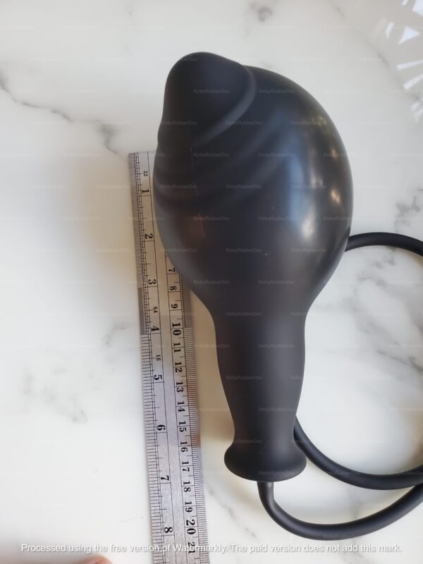 Large inflatable black silicone butt plug with size reference next to a ruler on a marble surface.