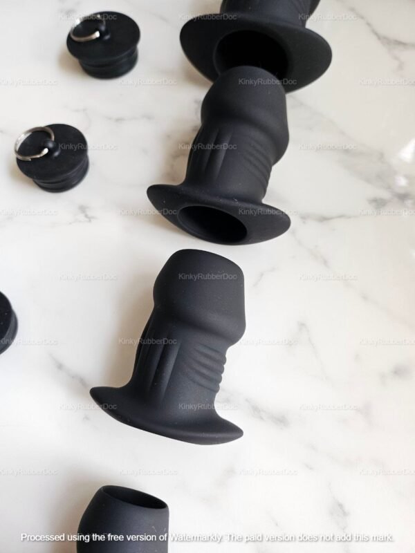 Black silicone tunnel plugs with stoppers on a marble surface.