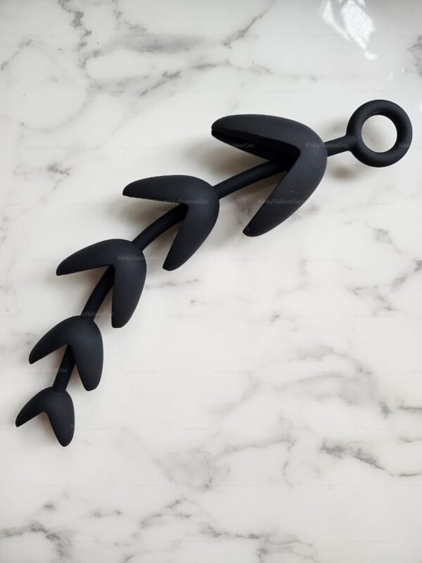 Full view of black claw-shaped silicone anal beads with pull ring on marble surface