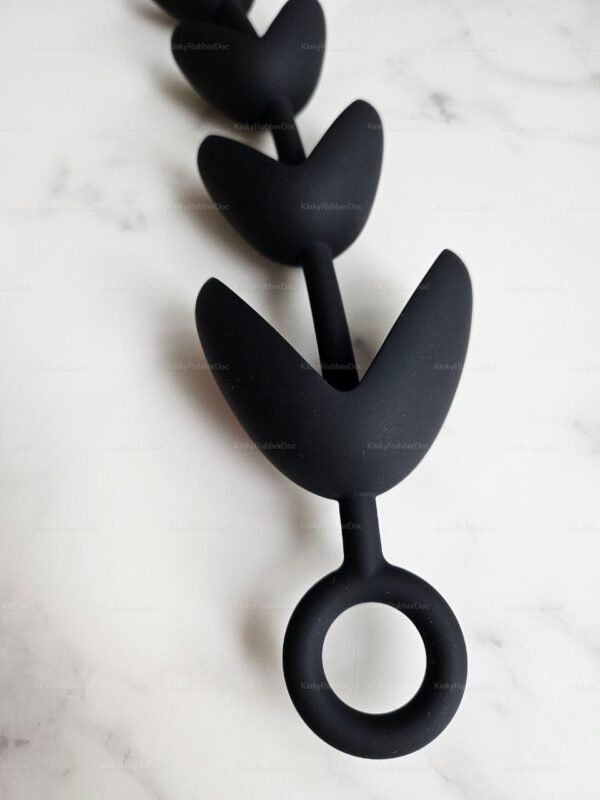 Black claw-shaped silicone anal beads with stretchable segments and a circular pull ring on a marble surface