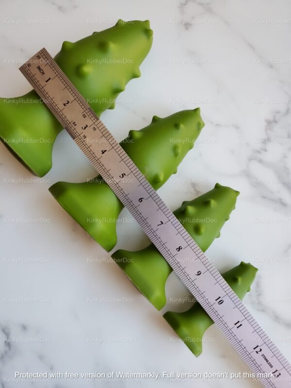 Green tree-shaped anal plugs in four sizes next to a metal ruler on white marble surface