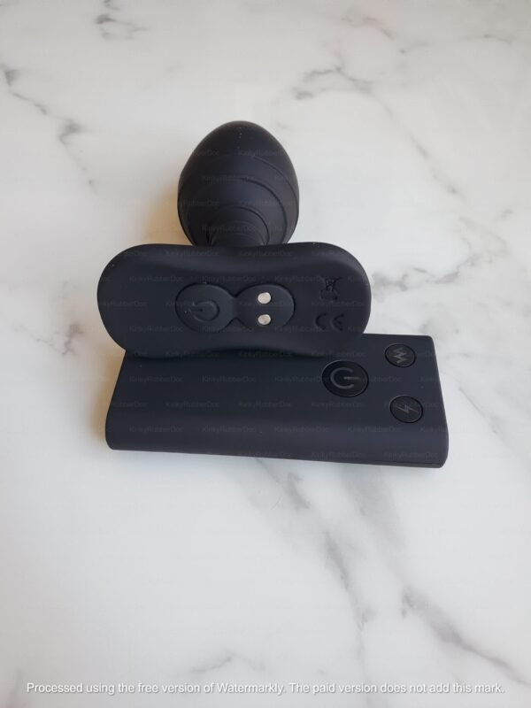 Rear view of black silicone electro anal plug with contact points and matching remote control on marble background
