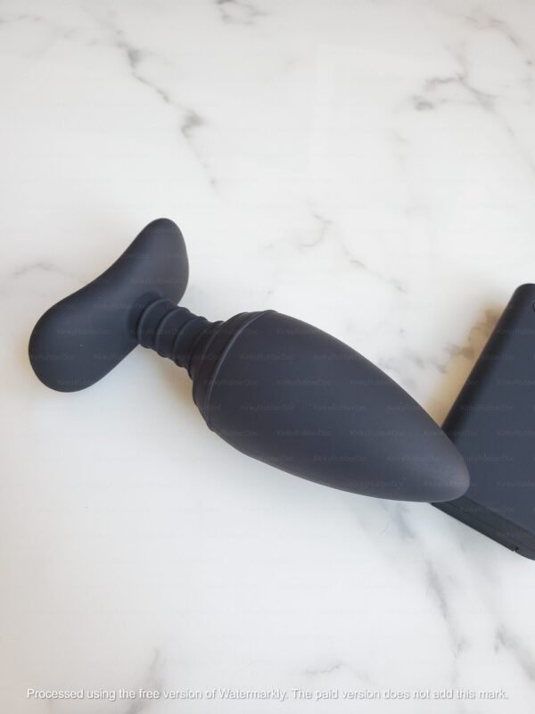 Close-up side view of sleek black electro anal plug with silicone texture on white marble surface