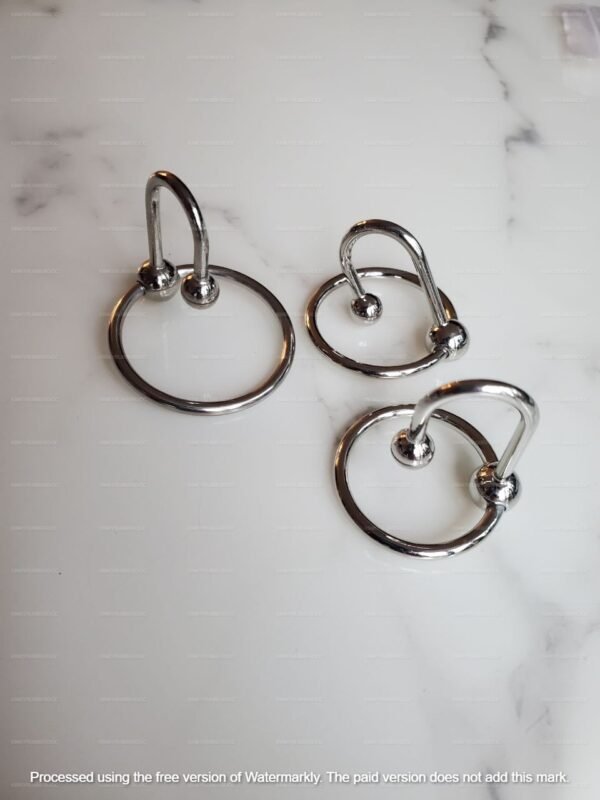 Shiny metal penis plug set with three size options featuring glans rings on a marble surface.
