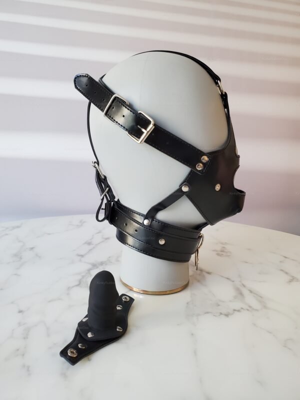 Black leather BDSM mask with adjustable straps and metal hardware on a marble surface.