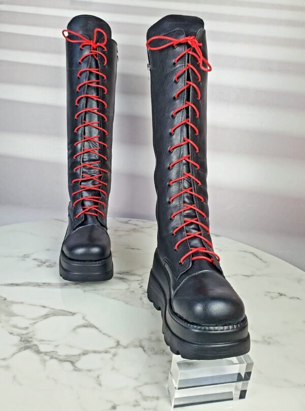 Black knee-high boots with red laces on a marble surface.