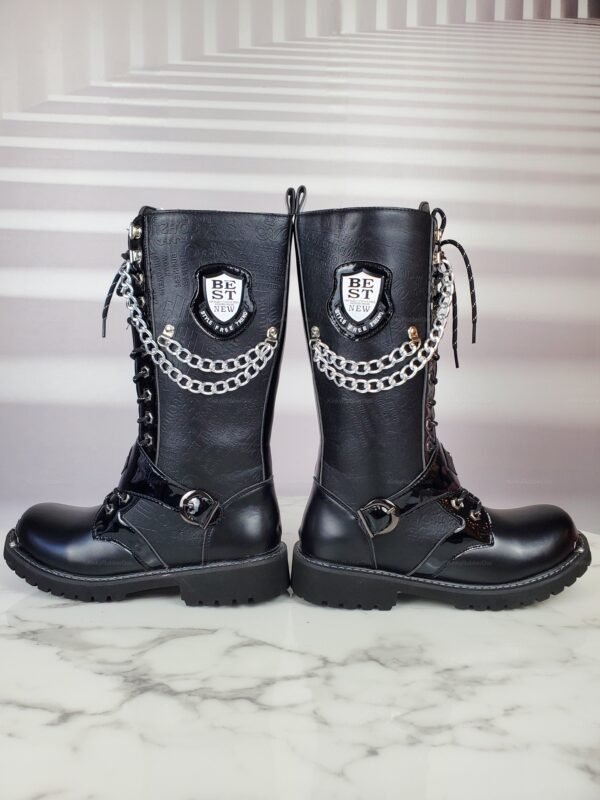 Black leather boots with chain detailing and bold badges, set on a marble surface.