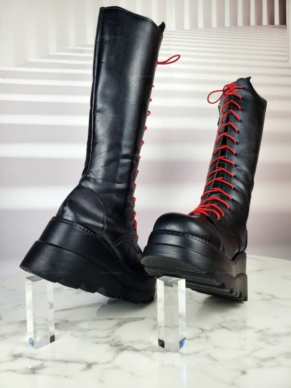 Sleek black knee-high boots with bold red laces, featuring chunky platform heels on a marble surface.