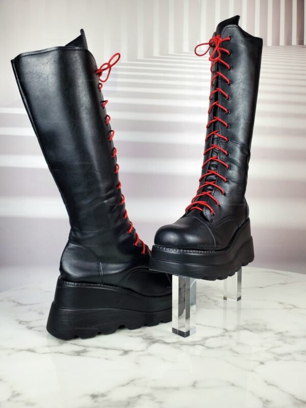 Black high-heel platform boots with red lace-up detailing on a marble surface.