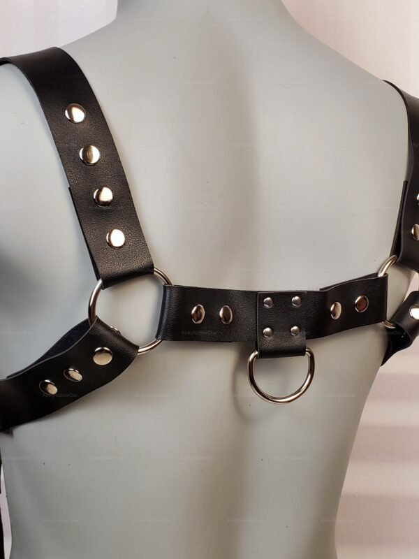 Back view of a black leather harness with metal ring connectors and rivet details.