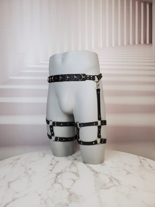 Black leather bondage-style waist and thigh harness on a marble surface.