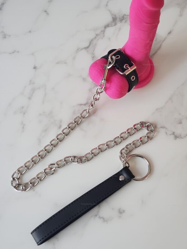 Leather cock stretcher with chain leash on marble surface.