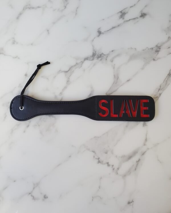 Black leather paddle with red lettering on a marble surface.