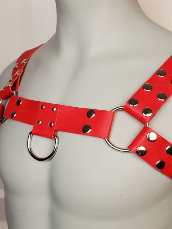 Angled view of red leather body harness with silver rivets and D-rings, queer clubwear accessory