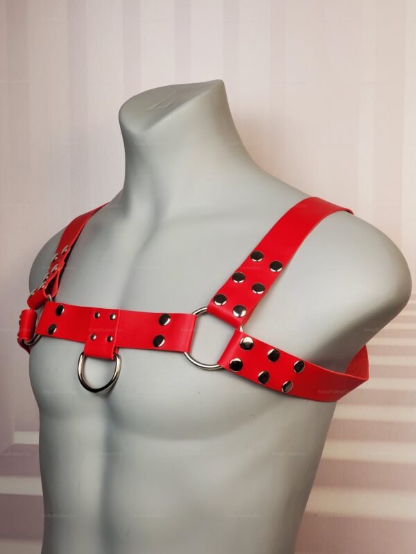 Angled view of red leather chest harness with D-rings and rivets, LGBTQ+ fetish fashion