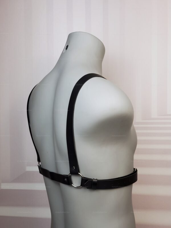 Simple black faux leather strap harness with silver O-rings worn on mannequin back, minimal BDSM gear