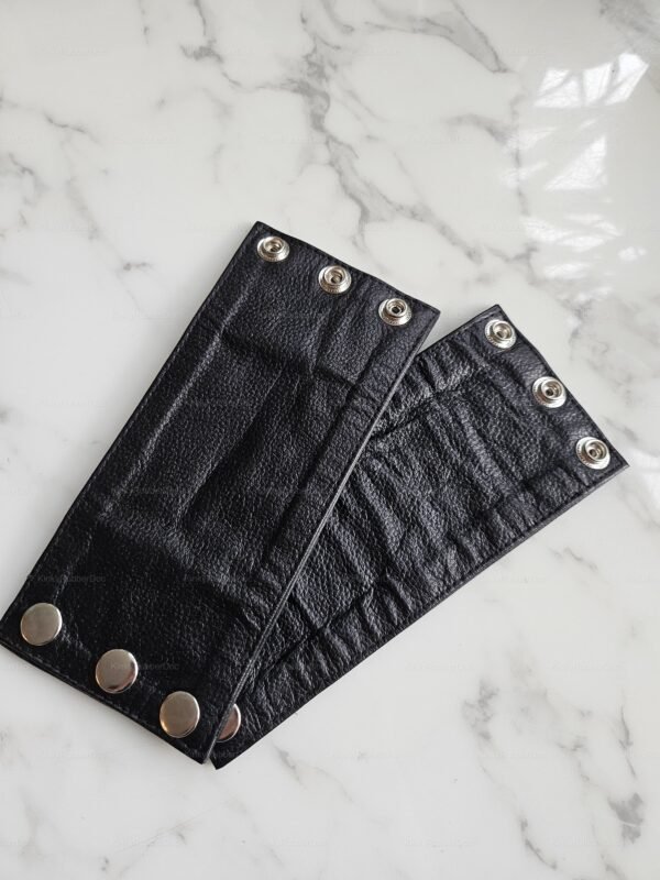 Black leather wristband with snap closure on a marble surface.