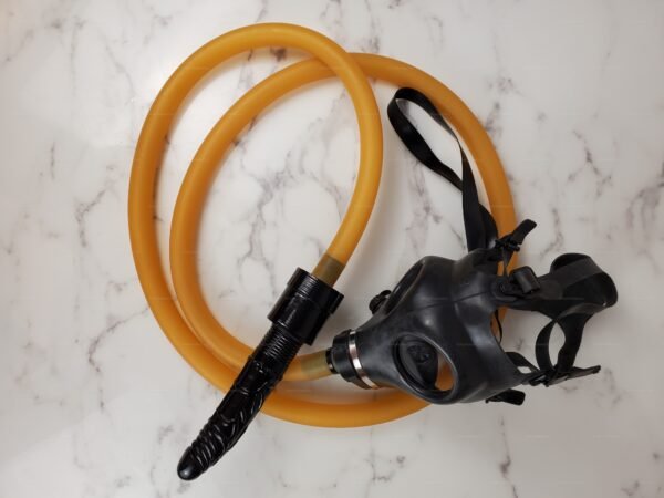A black dildo with a perforated base and hose connector, paired with a gas mask, resting on a marble surface.