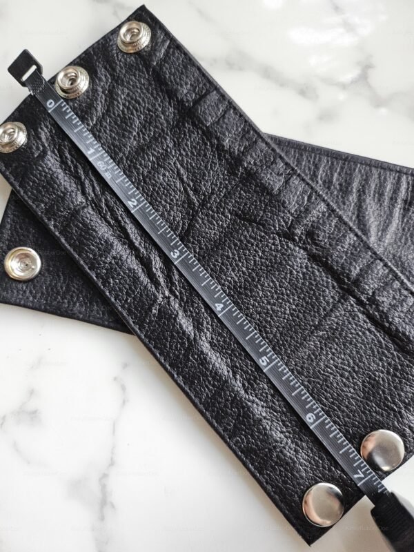 Black leather cuff with snap closures and textured finish, designed for a bold, edgy look.