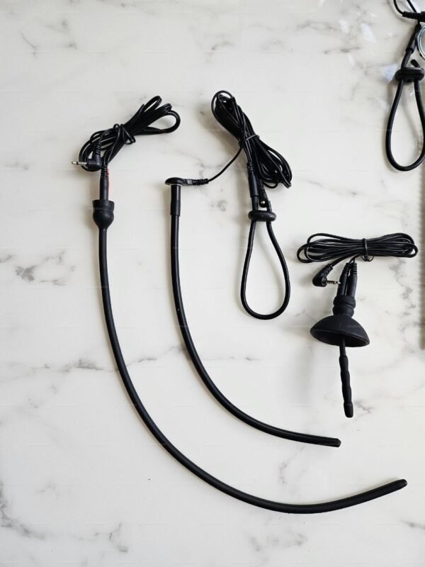 A set of electrosex urethral sound probes with black loops and wires laid out on a marble surface.