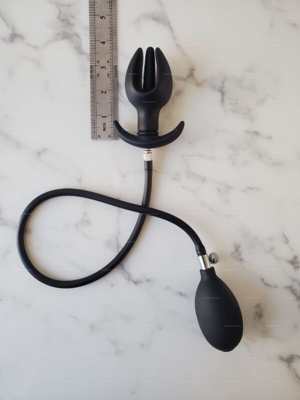 Close-up of a black flower-shaped butt plug expansion toy with inflatable feature and measuring ruler on a marble surface.