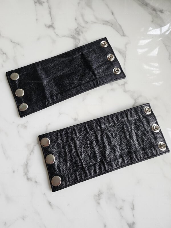Black handmade leather arm cuffs with snap closures on a marble surface.
