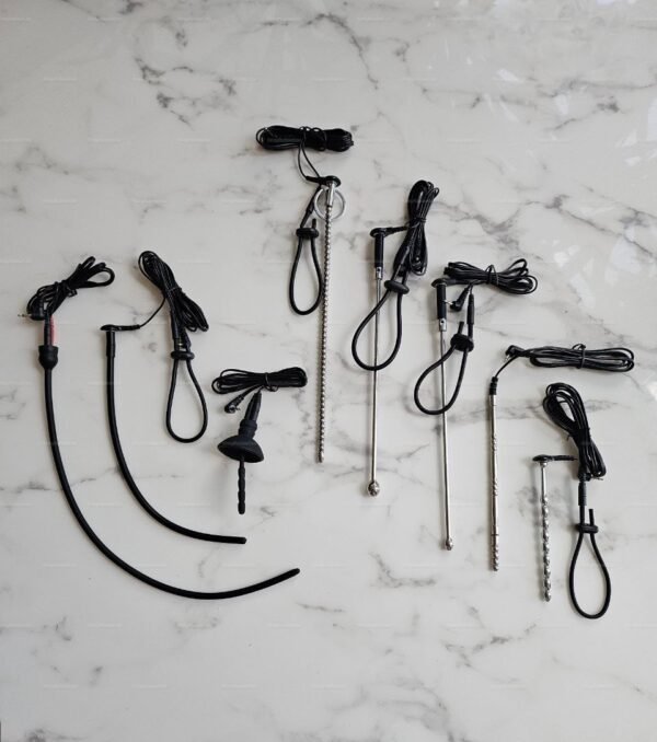 A collection of kinkyrubberdoc Electro Urethral Sound, sounding insertable tools laid out on a marble surface.
