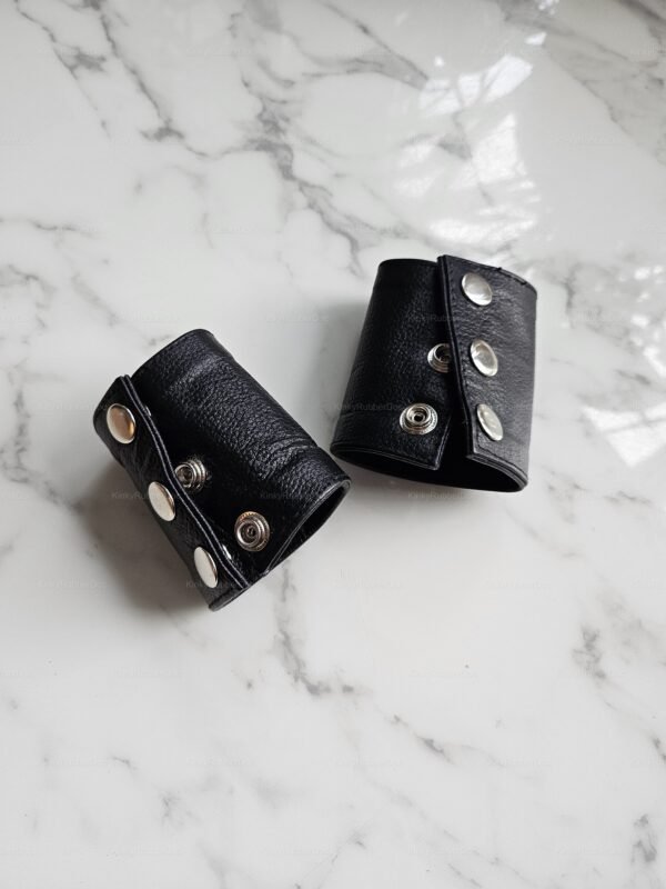 Black leather wrist cuffs with silver snaps on a marble surface.