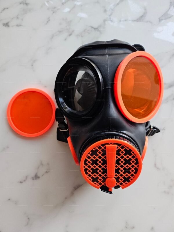 Black and orange gas mask with a distinctive warning valve design, featuring bold colors and a unique aesthetic.