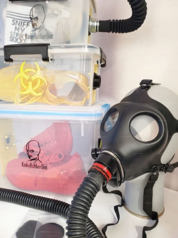 A black rubber mask with a flexible hose and RD40 port, connected to a clear storage box labeled "KinkyRubberDoc," designed for sensory exploration.