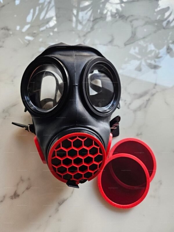 Black gas mask with red honeycomb grill and red lens accents on marble surface.