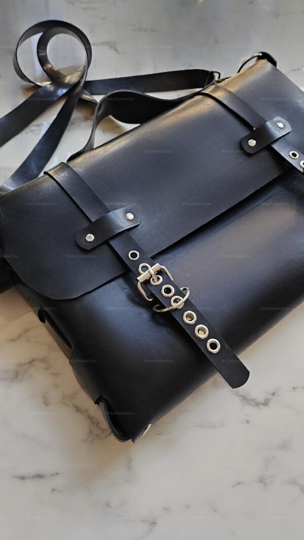Sleek black rubber handbag with a shoulder strap and metal buckle details on a marble surface.