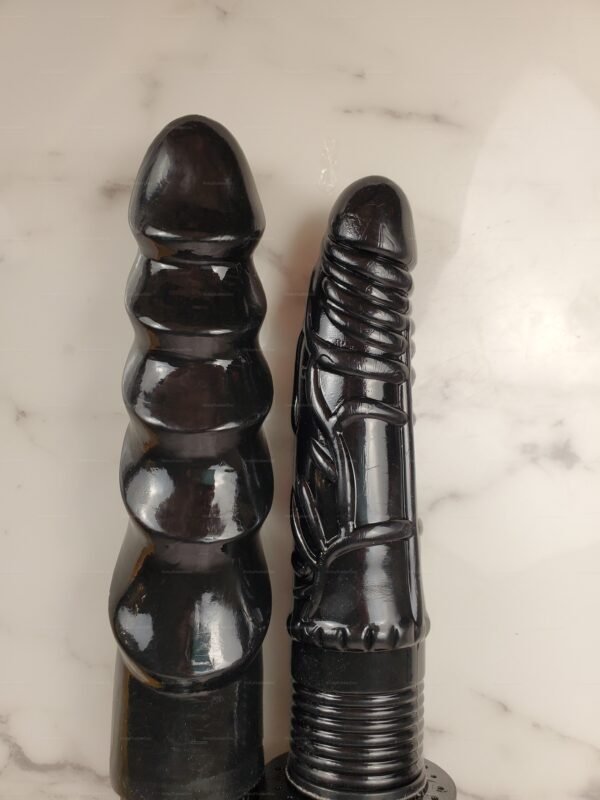 Two intricately designed black silicone dildos on a marble surface, featuring unique textures and shapes for sensory exploration.