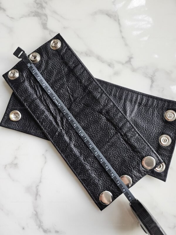 Black leather wrist-wrap cuff with metallic snaps, featuring a textured surface and sleek design.